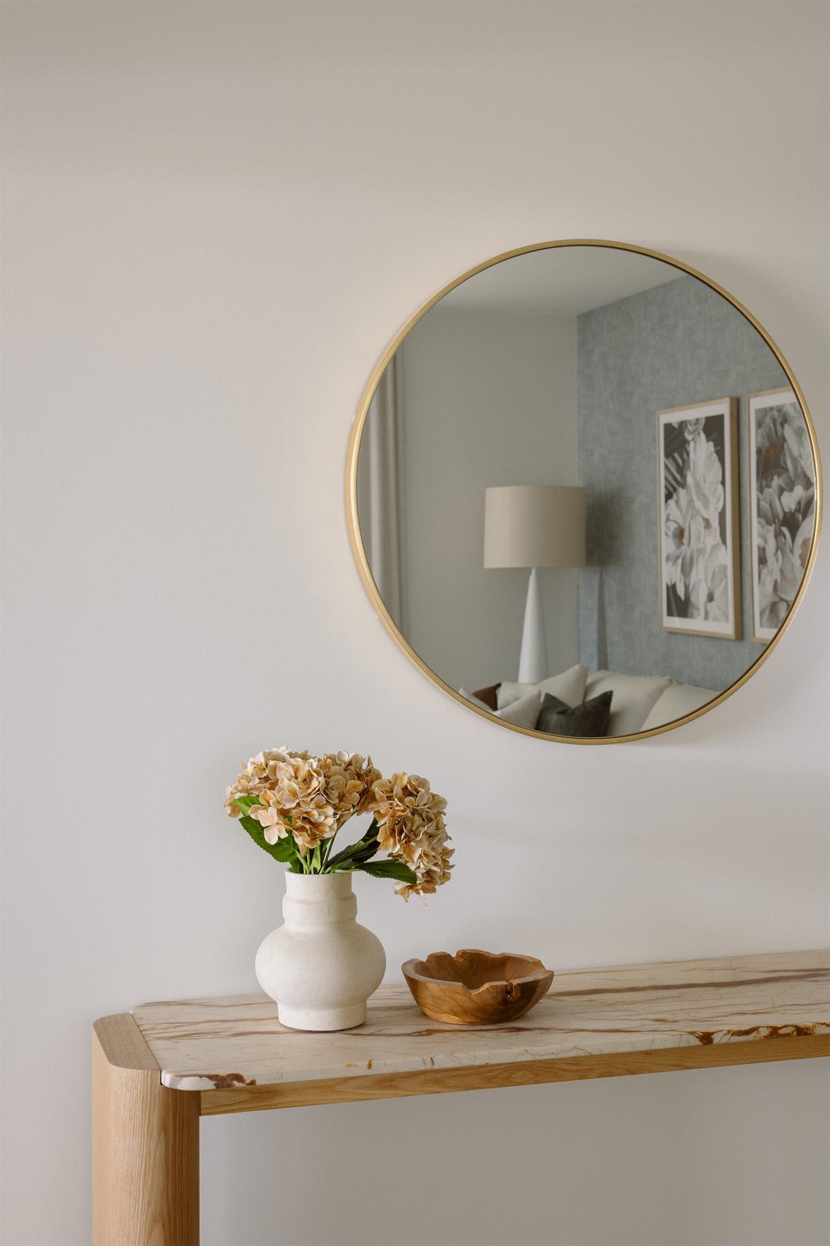 Round brass mirror above a marble console with dried hydrangeas